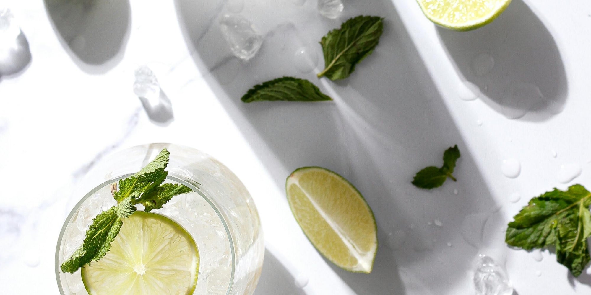 Glass of artisan gin with lime wedges and mint leaves on a white background