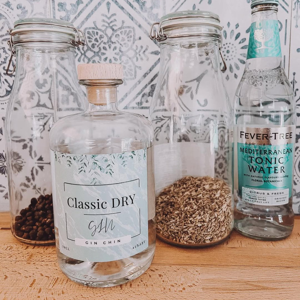 Bottles of 'Classic Dry' Gin Chin gin and 'Fever-Tree Mediterranean Tonic Water' on a wooden surface with a decorative tile background.