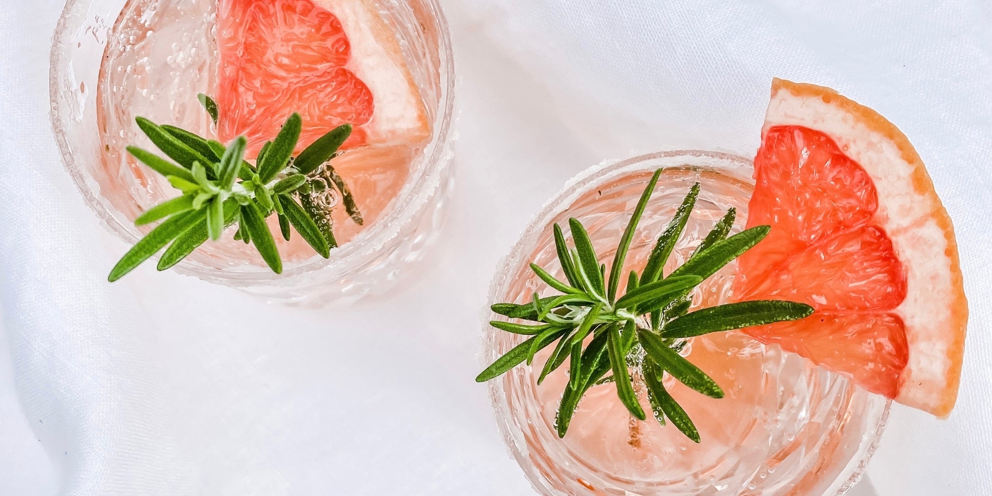 Two craft gin cocktails with grapefruit slices and rosemary on a white background