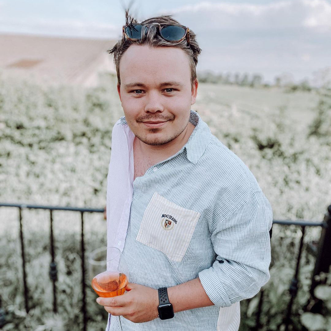 Man standing outdoors with a field in the background, sipping a glass of small batch gin