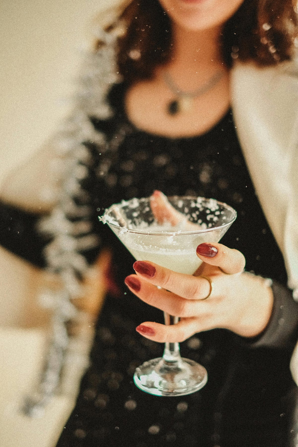 Person holding a cocktail in a martini glass with a blurred background