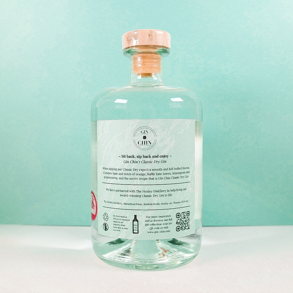 Clear glass bottle of Gin Chin Classic Dry Artisan Gin with a label on a light blue background