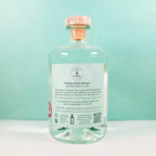 Clear glass bottle of Gin Chin Classic Dry Artisan Gin with a label on a light blue background