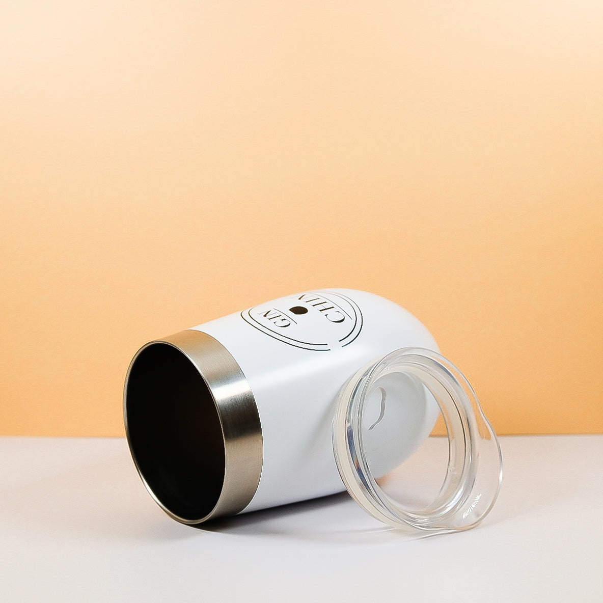White insulated travel tumbler with a clear lid on a light peach background