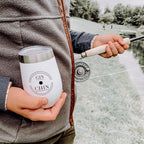 Person holding a white travel tumbler with 'Gin Chin' branding and a fishing rod by a body of water.