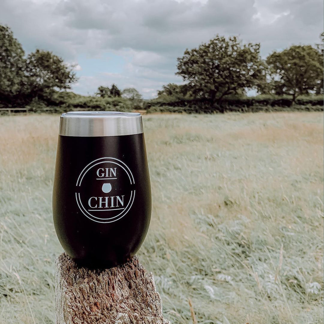 Black insulated gin tumbler with 'GIN CHIN' logo on a wooden post in a field