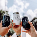 Three black and white 'GIN CHIN' insulated gin tumblers held by hands against a blurred outdoor background.