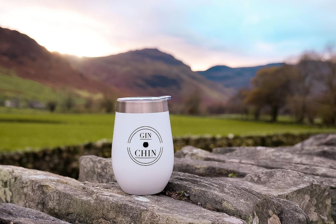 White insulated gin tumbler with 'GIN CHIN' branding on a stone wall with a scenic background
