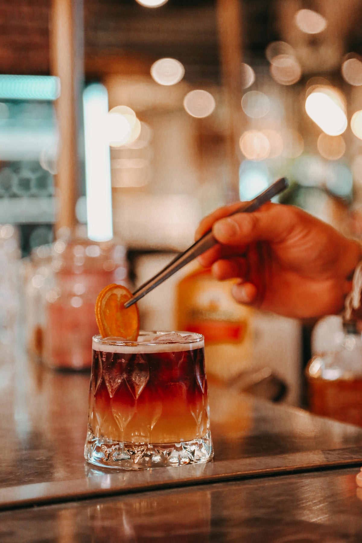 Person garnishing a gin cocktail with an orange peel in a bar setting