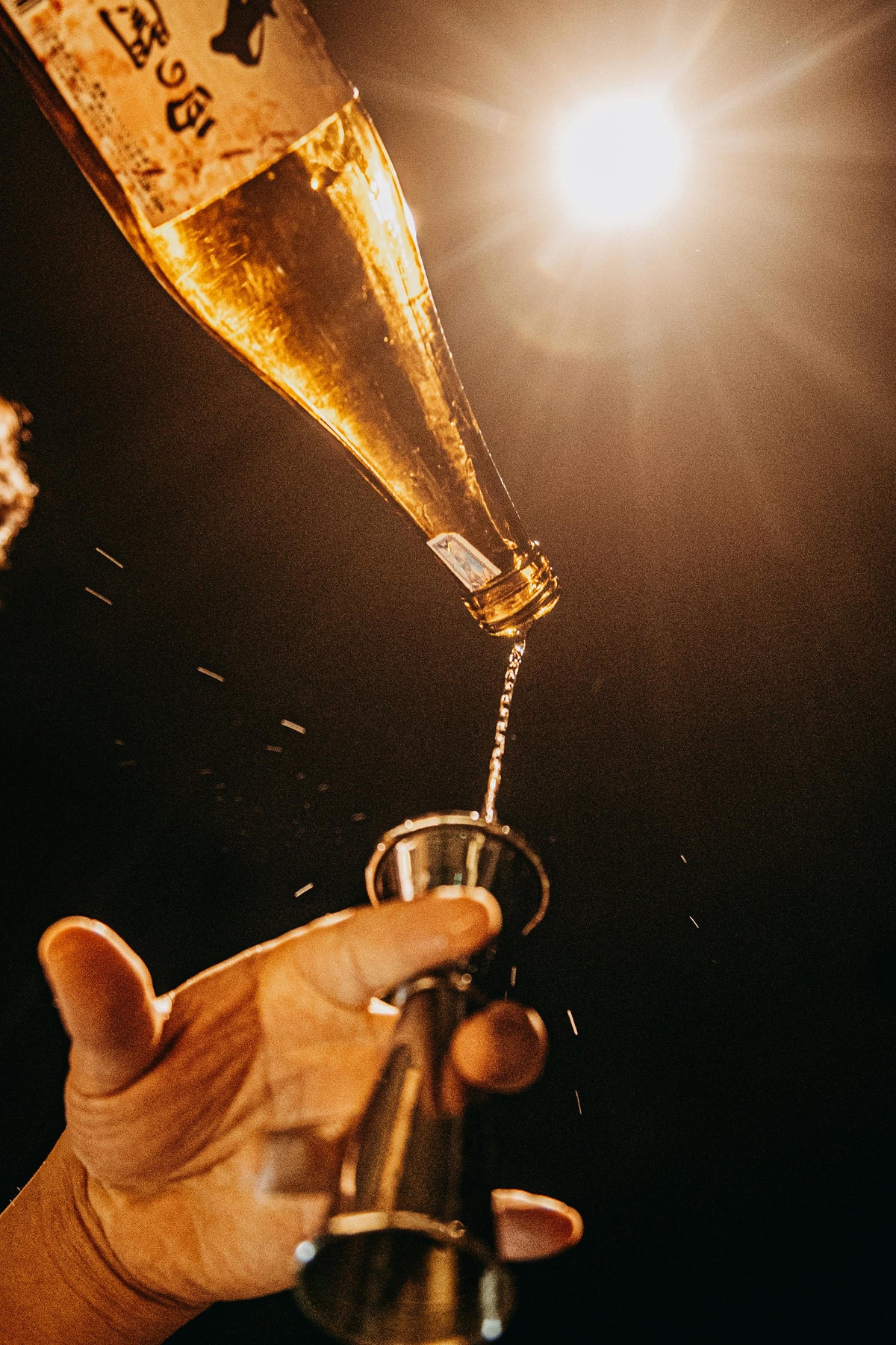 Hand pouring champagne from a bottle into a glass against a dark background