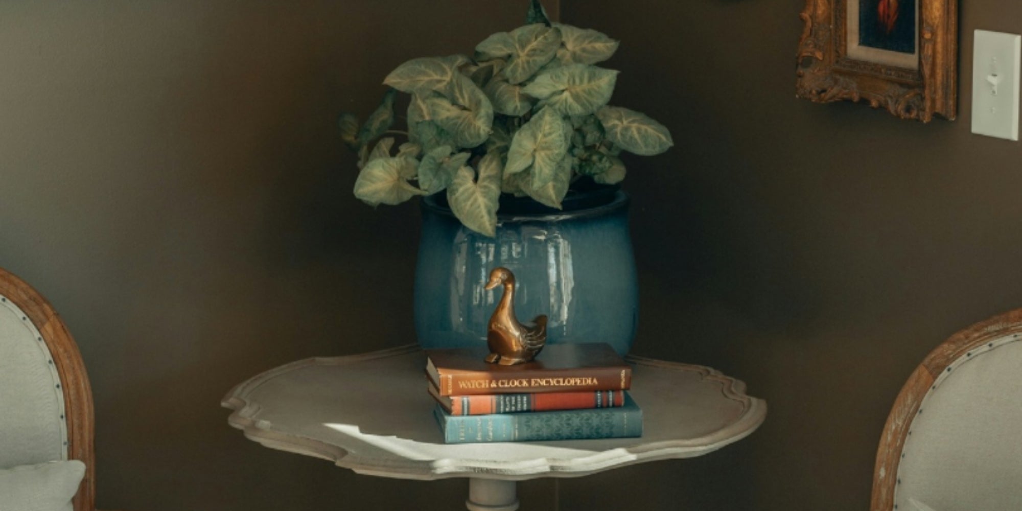 Decorative table with a vase, books, and plant against a dark wall.