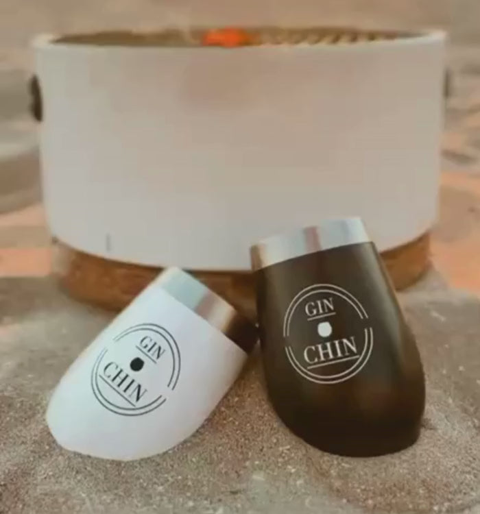 Two insulated gin cups, one white and one black, with 'Gin Chin' branding on sand